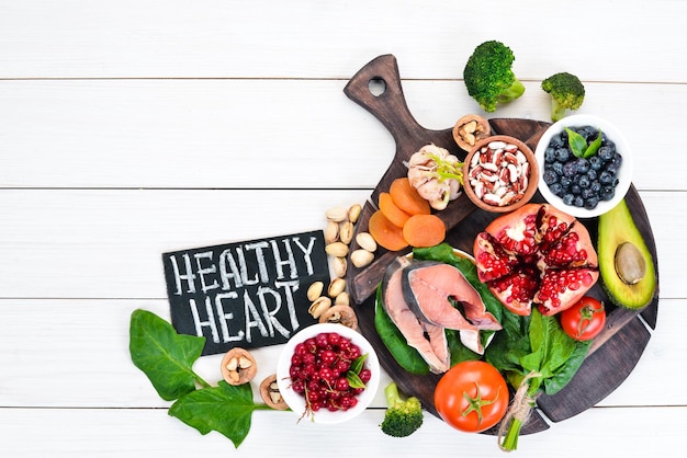 Healthy food for the heart Fish blueberries nuts pomegranate avocados tomatoes spinach flax On a white wooden background Top view