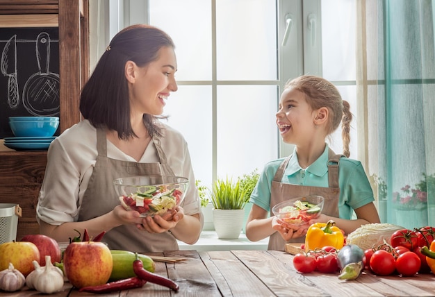 家庭での健康食品。キッチンで幸せな家族。母と子の娘が野菜や果物を準備しています。