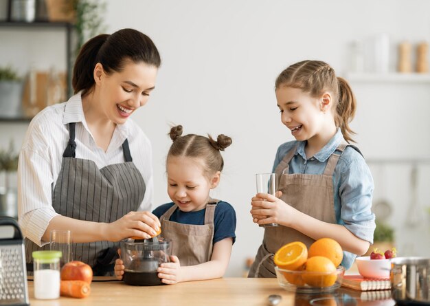 家庭での健康食品キッチンで幸せな家族母と子供たちはオレンジジュースを準備しています