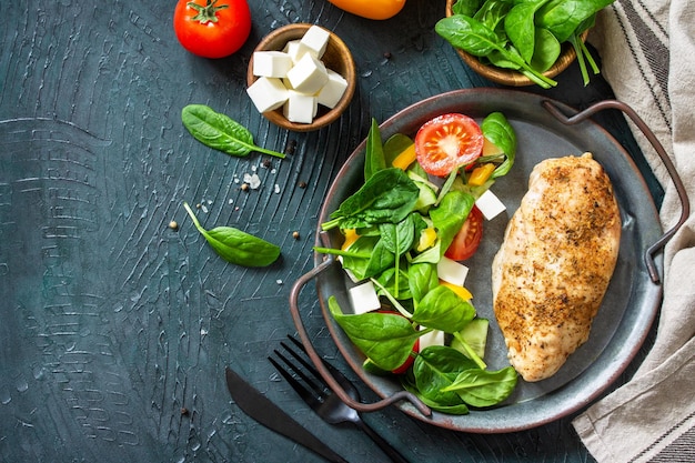 健康食品ケトジェニックダイエットランチダークストーンの背景に新鮮な野菜のサラダほうれん草とフェタチーズを添えたチキンフィレのグリル上面図フラットレイコピースペース