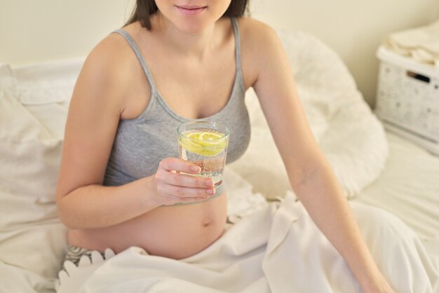 사진 건강 식품 라이프 스타일, 임신 한 젊은 여성이 침대에서 집에 앉아 레몬 슬라이스로 식수