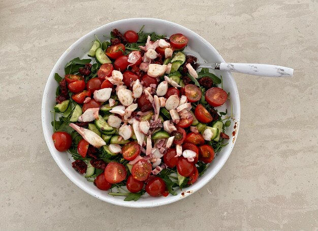 Foto alimentazione sana dieta mediterranea insalata di polpo pomodoro arugula in una ciotola con un cucchiaio