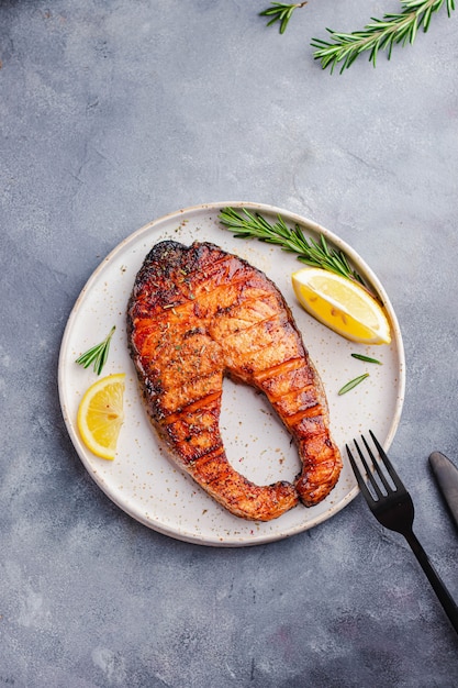 Healthy food omega concept. grilled salmon steak with lemon, rosemary served on white plate on gray stone