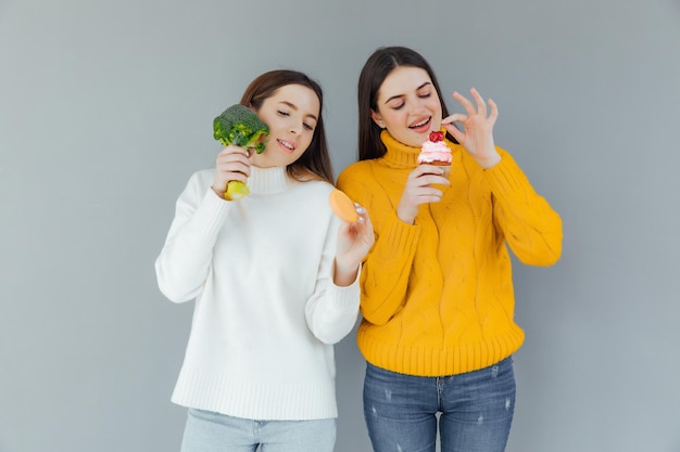 Healthy food. One woman is holding broccoli and the other a cake