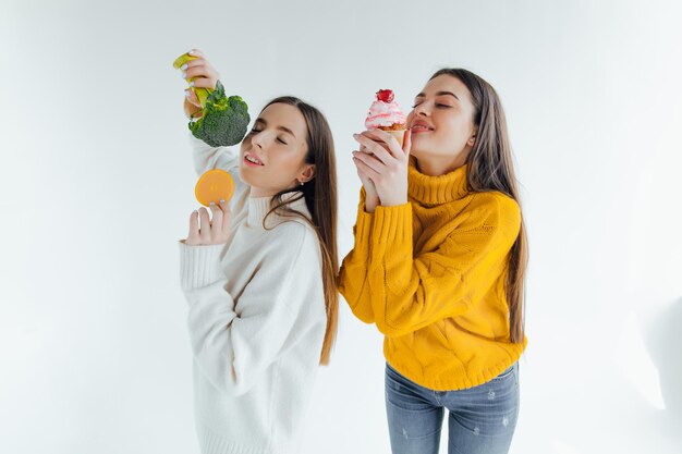 Healthy food. One woman is holding broccoli and the other a cake