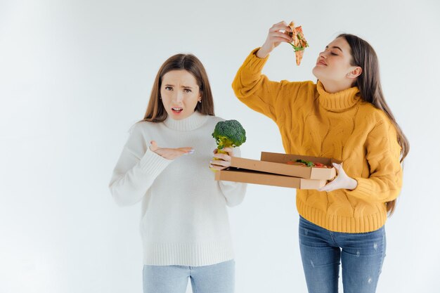 Healthy food. One woman is holding a pizza and the other a broccoli