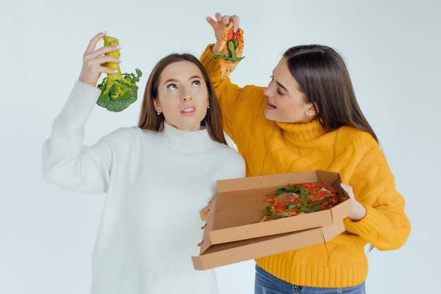 Healthy food. One woman is holding a pizza and the other a broccoli
