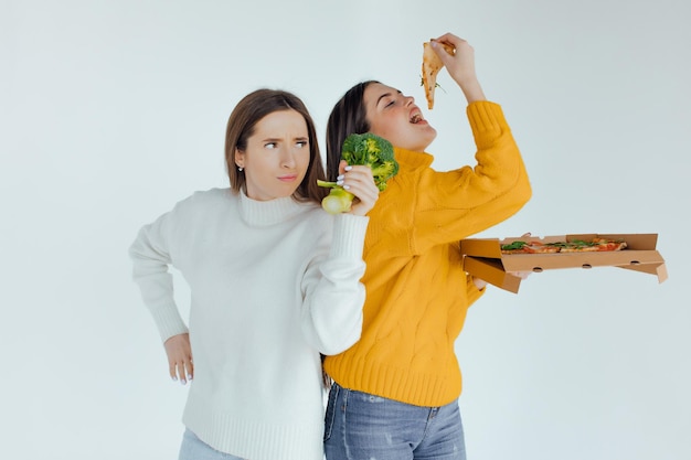 Healthy food. One woman is holding a pizza and the other a broccoli