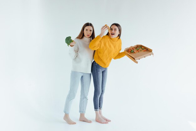 건강한 음식. 한 여성은 피자를 들고 다른 여성은 브로콜리를 들고 있습니다.