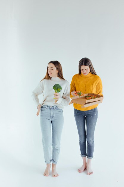 Healthy food. One woman is holding a pizza and the other a broccoli