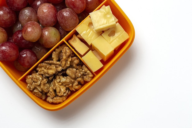 Cibo sano in contenitori di plastica pronti da mangiare con formaggio, uva e noci sul tavolo di lavoro. per portare via le noci. isolato