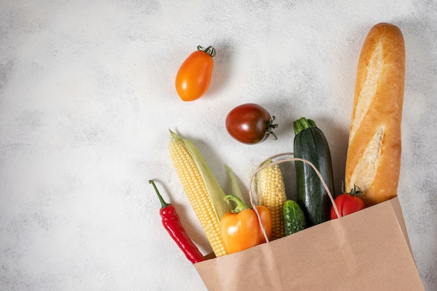 健康食品の選択。新鮮な野菜がいっぱい入った買い物袋の紙。フラットはテーブルの上に食べ物を置きます。