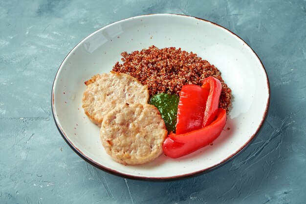 Photo healthy food - steamed chicken burgers (cutlets) with quinoa and pesto sauce in a white bowl on a gray background
