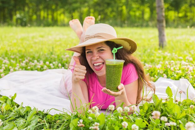 Концепция здорового питания, лета и людей - молодая женщина веселится в парке и пьет зеленые коктейли на пикнике