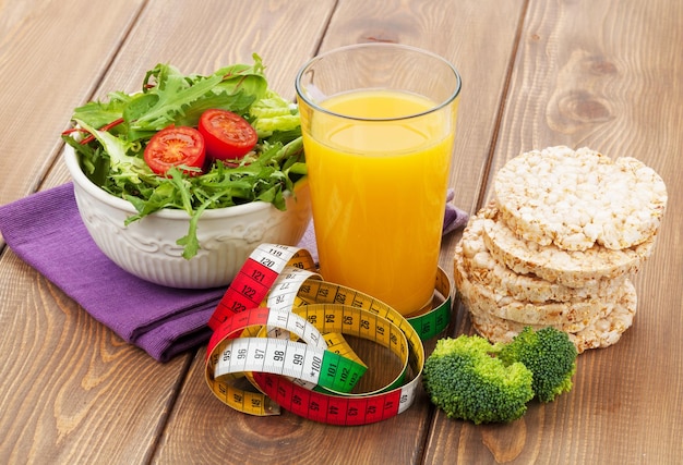 Healthy food and tape measure over wooden table