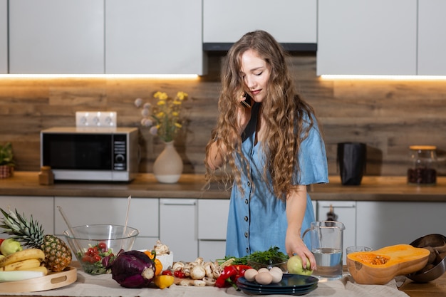 Photo healthy food - vegetable salad. diet. dieting concept. young curly woman preparing vegetable salad in her kitchen , talking on the mobile phone and smiling while . healthy lifestyle concept.