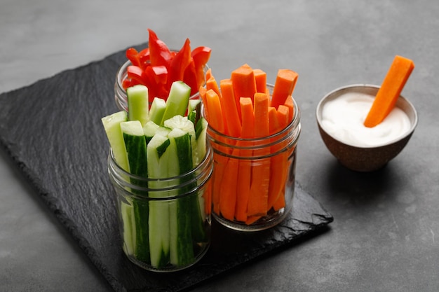 Healthy food vegetable sticks in glass jars with white sauce on black board