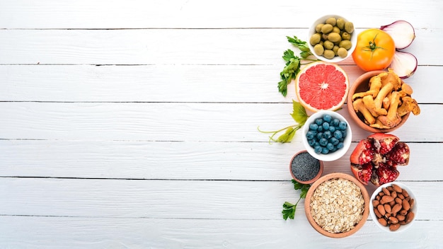 Healthy food on a white wooden table Fresh vegetables fruits nuts berries mushrooms Top view Free space for text