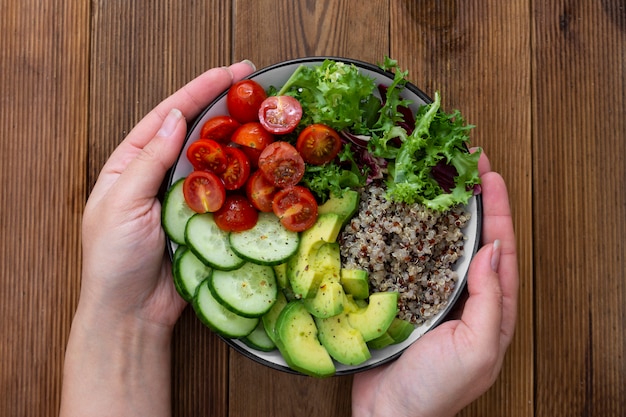 Healthy food. Womans hand holding budha bowl with quinoa, avocado, cucumber, salad, tomatoe, olive oil. 