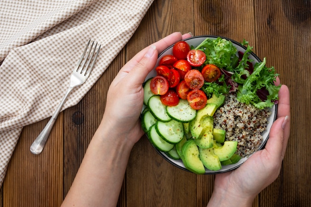 Healthy food. Womans hand holding budha bowl with quinoa, avocado, cucumber, salad, tomatoe, olive oil. 