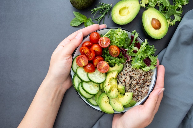 Healthy food. Womans hand holding budha bowl with quinoa, avocado, cucumber, salad, tomatoe, olive oil. 