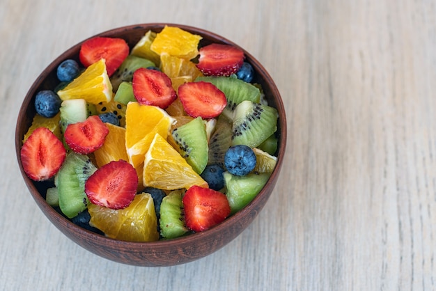 Healthy fresh fruit salad in bowl on light.