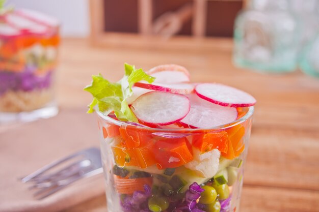 Healthy fresh salad in glassful with red cabbage, tomato, quinoa, green salad and radish on the wooden table