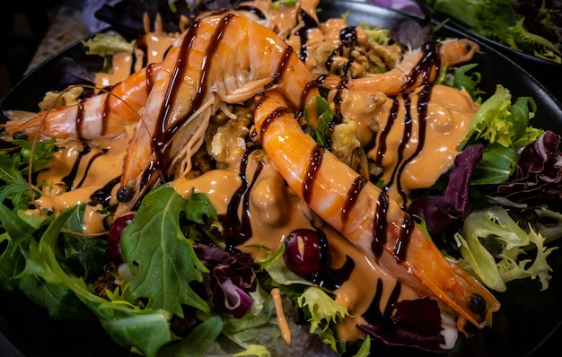 Healthy and fresh salad with shrimps and vegetables serving on the plate on a table in a restaurant with decor. Beautiful appetizer langoustines with rukola.