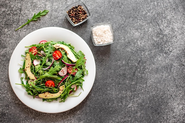 Insalata di verdure fresche sane pomodori rucola avocado ravanello su uno sfondo di pietra