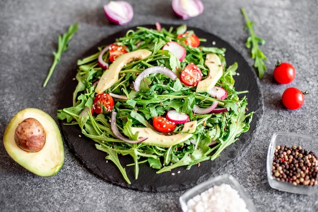 Healthy fresh vegetable salad tomatoes arugula avocado radish on a stone background