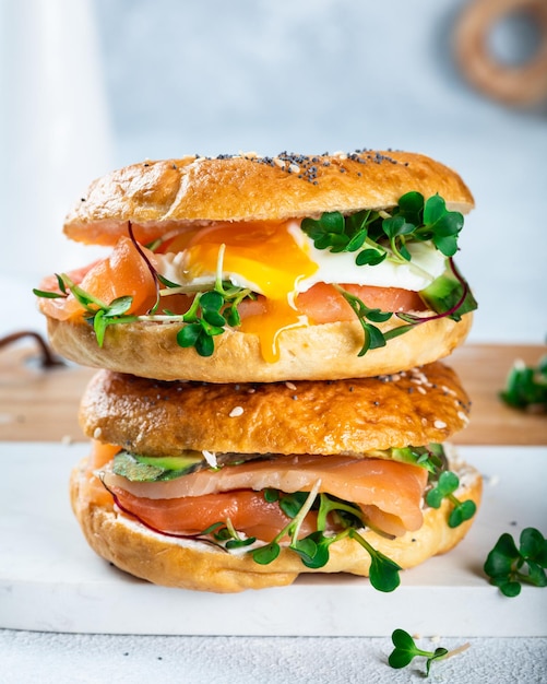 Healthy freshly baked bagel filled with salmon, microgreen, avocado and egg. Served on white desk. Sandwich with salmon. Healthy breakfast.