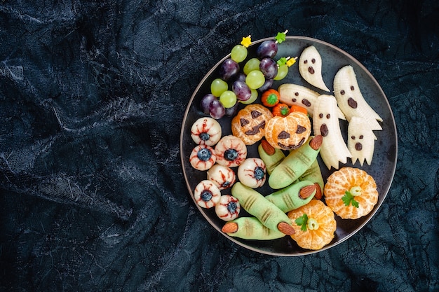 건강한 과일 할로윈 취급합니다. 바나나 유령, 클레멘 타인 오렌지 호박, 열매 눈 및 녹색 마녀 손가락 쿠키