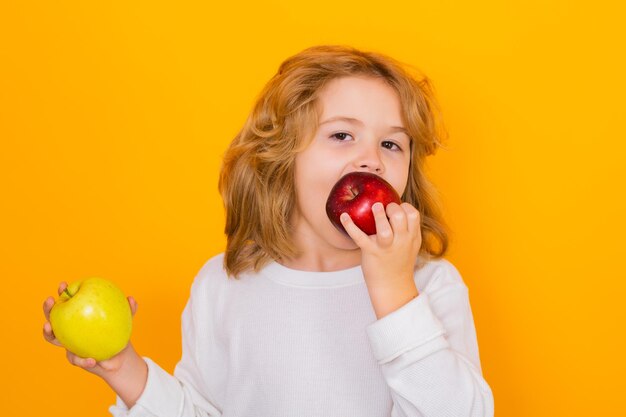 黄色の背景に分離されたリンゴを保持するかわいい子のスタジオの肖像画のスタジオでアップルと子供の子供のための健康的な果物