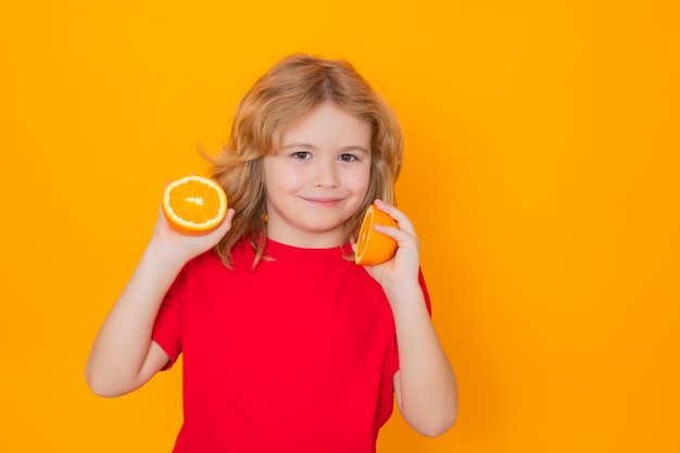 子供のための健康的な果物 スタジオでオレンジを持つ子供 かわいい子のスタジオ ポートレートは、黄色の背景に分離されたオレンジを保持します