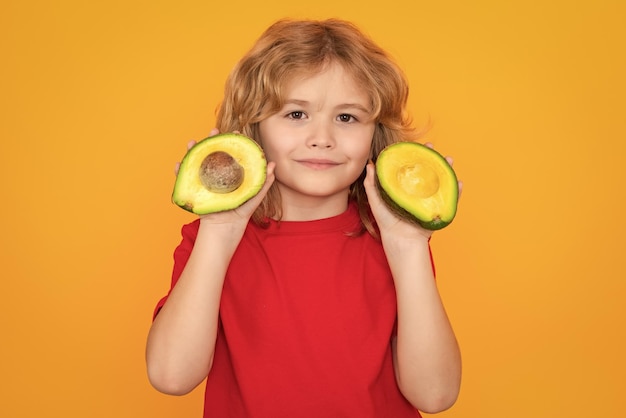 Healthy fruits and vegetables for kids kid hold red avocado in studio studio portrait of cute child with avocado isolated on yellow background