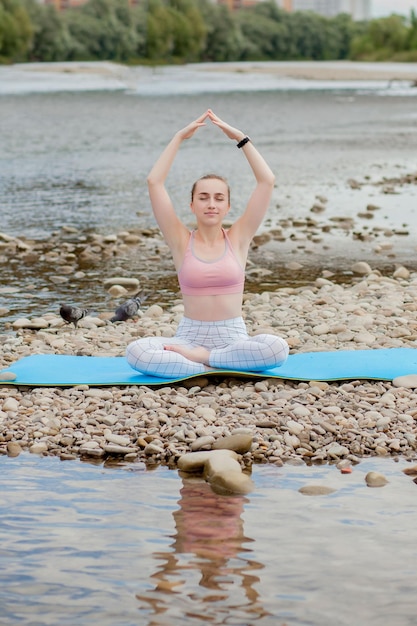 Здоровая девушка расслабляется во время медитации и делает упражнения йоги в красивой природе на берегу реки