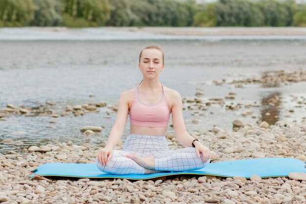 Healthy girl relaxing while meditating and doing yoga exercise in the beautiful nature on the bank of the river