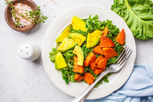 Healthy green kale salad with avocado and baked sweet potatoes. 