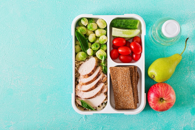 Healthy green meal prep containers with chicken fillet, rice, brussels sprouts and vegetables overhead shot with copy space. Dinner in lunch box. Top view. Flat lay