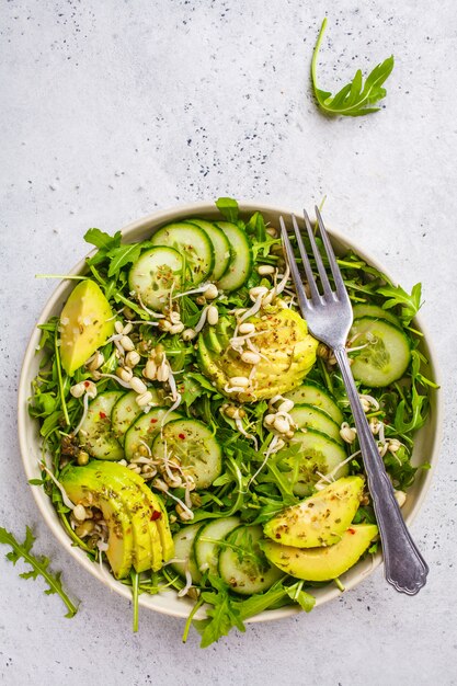 Healthy green salad with avocado, cucumber and arugula in white dish