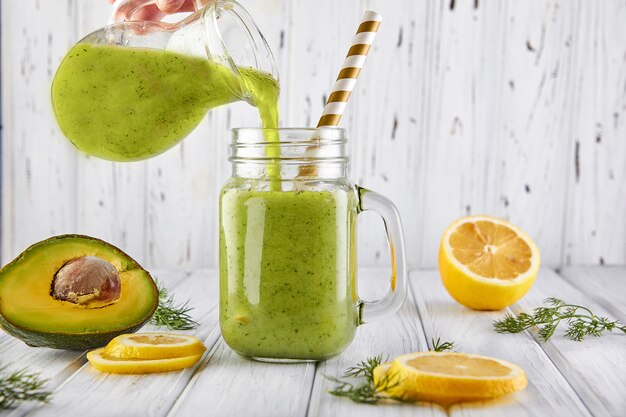 A healthy green smoothie is poured from a jug into a jar. Green smoothie with organic ingredients, vegetables