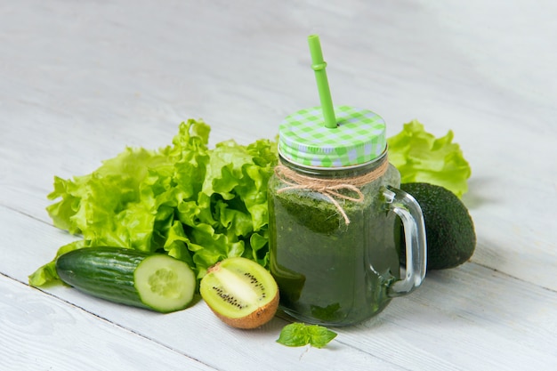 Healthy green smoothie with ingredients on white wooden background