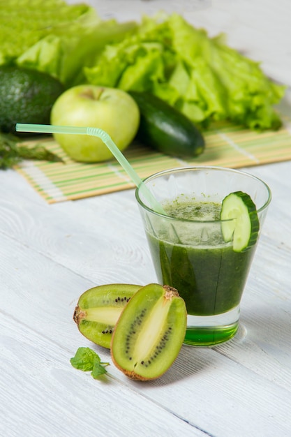 Healthy green smoothie with ingredients on white wooden table