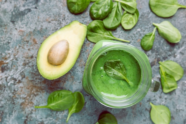 Healthy green smoothie with spinach, avocado, banana and chia seeds in glass jars on gray stone background, top view.