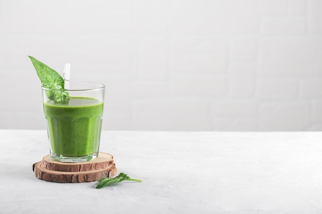 Healthy green smoothie with spinach banana and vegan milk in glass on light grey background copy