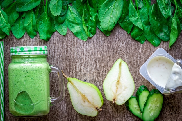 Healthy green smoothie with spinach in a mug against on wooden background