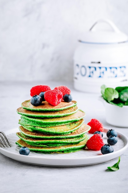 Healthy green spinach pancakes with raspberries blueberries and honey for breakfast