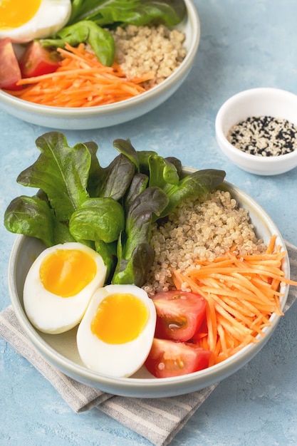 Healthy green vegetarian buddha bowl lunch with eggs, quinoa, carrots,tomato, lettuce leaves, on a blue background. vertical format