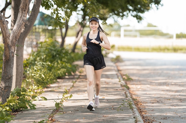 Una sana e felice donna asiatica runner in abiti sportivi neri che fa jogging nel parco naturale della città sotto il tramonto serale