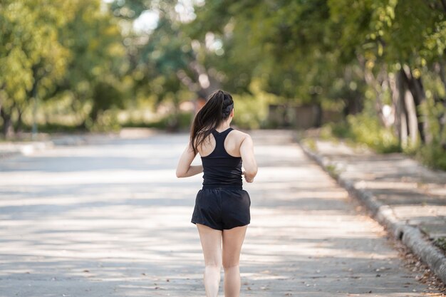 Здоровая счастливая азиатская бегунья в черной спортивной одежде бегает трусцой в природном городском парке под вечерним закатом